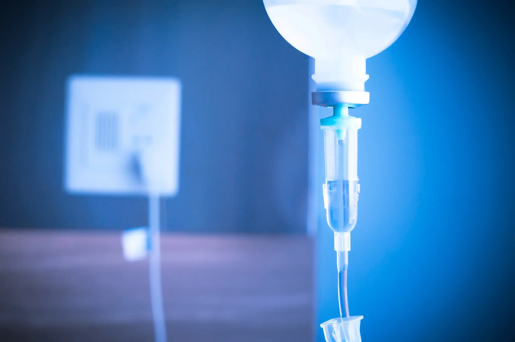 saline drip with iv tubing against a blue hospital background